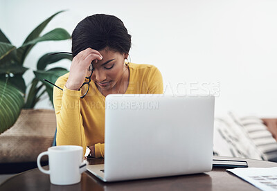 Buy stock photo Shot of an attractive young woman sitting alone at home and suffering from a headache while using her laptop