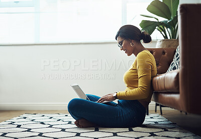 Buy stock photo Full length shot of an attractive young woman sitting alone at home and using her laptop