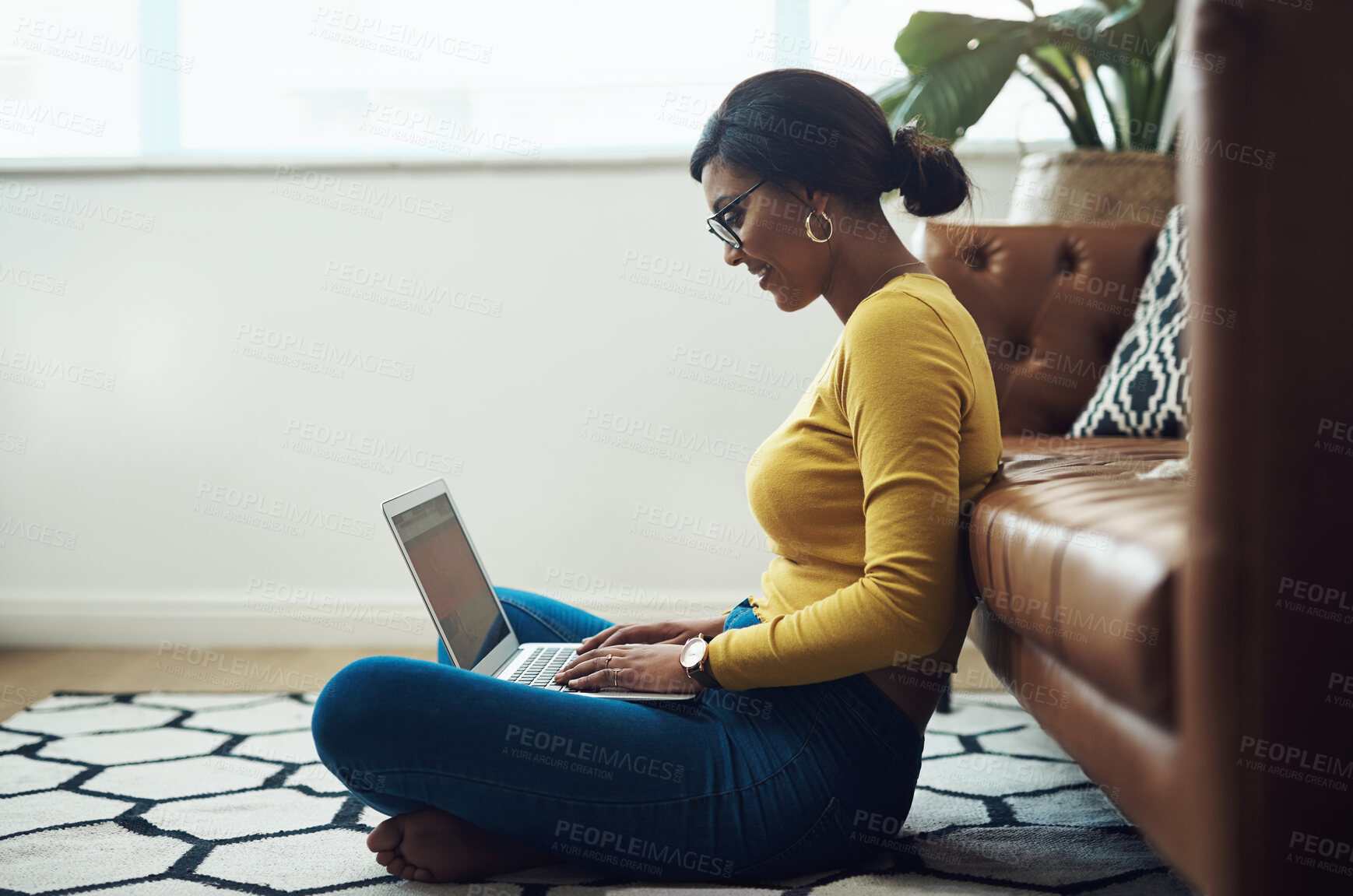 Buy stock photo Full length shot of an attractive young woman sitting alone at home and using her laptop