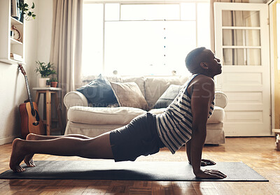 Buy stock photo Shot of a sporty young man doing a cobra stretch while exercising at home