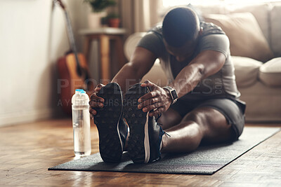 Buy stock photo Shot of a sporty young man stretching his legs while exercising at home