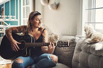 Buy stock photo Shot of a young woman playing a guitar on a relaxing day at home