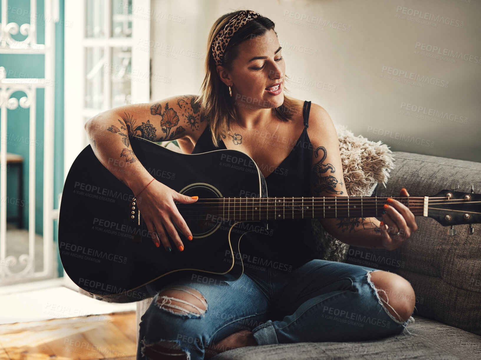 Buy stock photo Shot of a young woman playing a guitar on a relaxing day at home