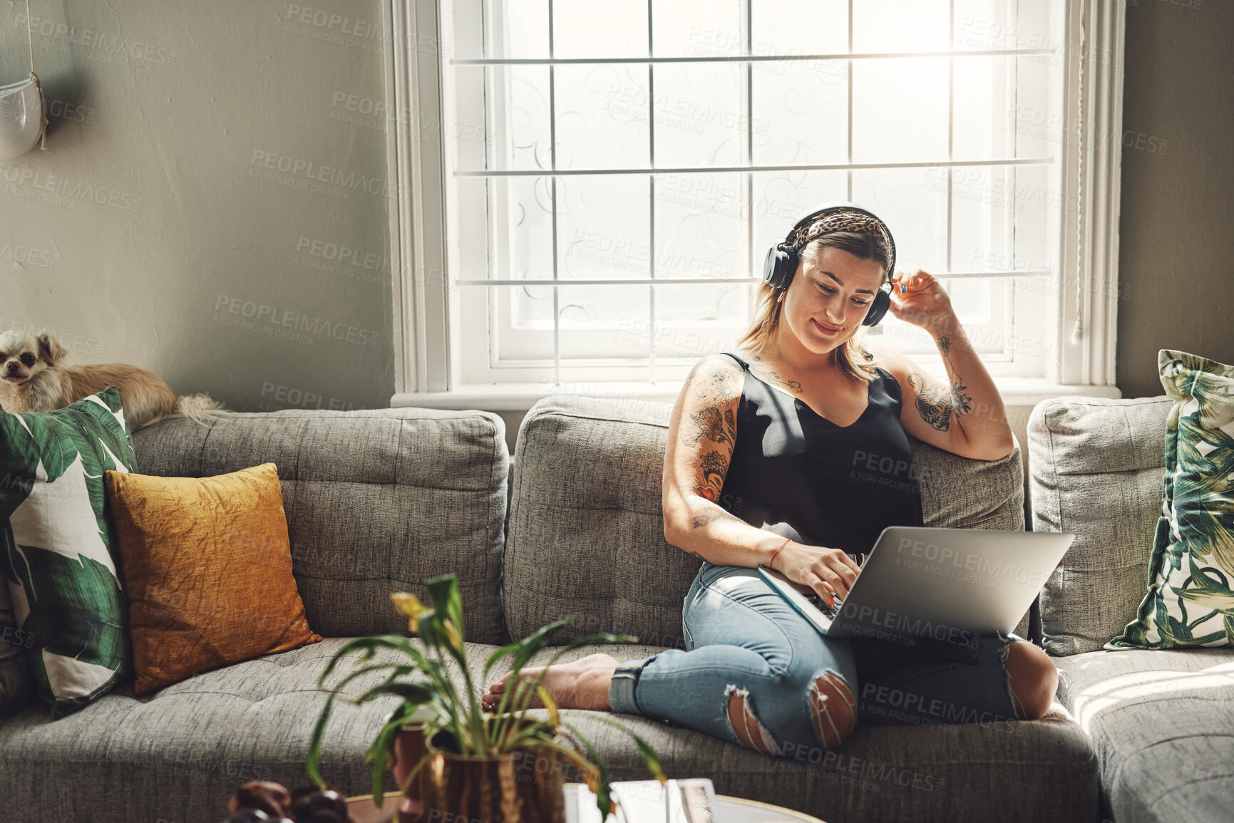 Buy stock photo Shot of a young woman using a laptop and headphones on the sofa at home
