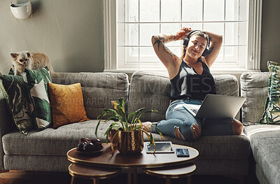 Buy stock photo Shot of a young woman using a laptop and headphones on the sofa at home