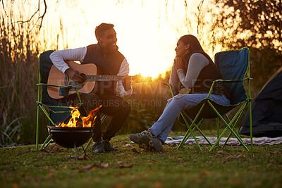 Buy stock photo Shot of a young man serenading his girl while playing guitar during a camping trip