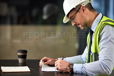 Buy stock photo Cropped shot of a handsome mature male construction worker filling out paperwork at his desk in the office