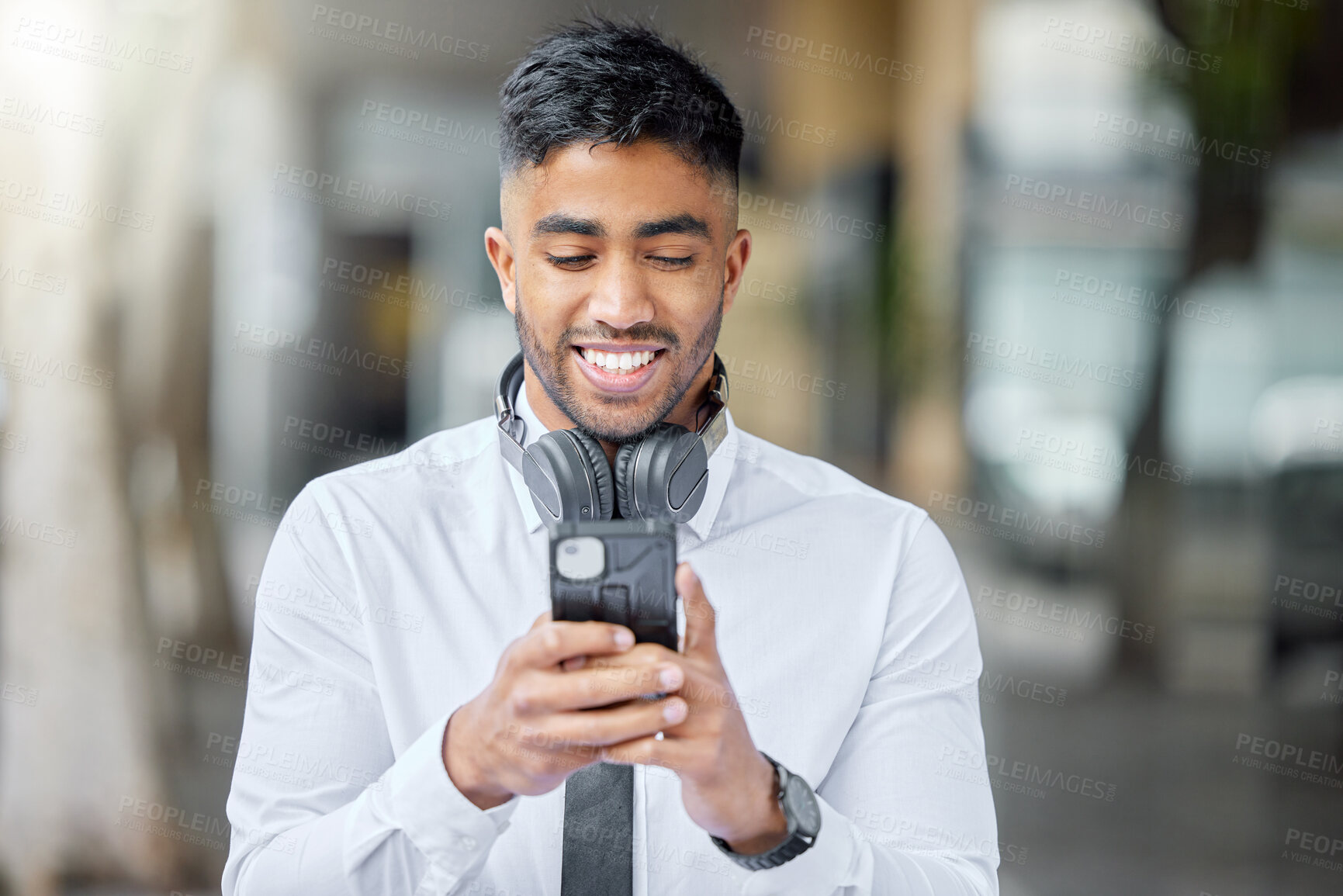 Buy stock photo Business man, phone text and city of a professional with headphones watching a video. Urban, smile and Indian male person with work travel, mobile streaming and happiness with cellphone app and web