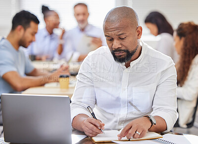 Buy stock photo Shot of a mature businessman writing notes while working on a laptop in an office with his colleagues in the background