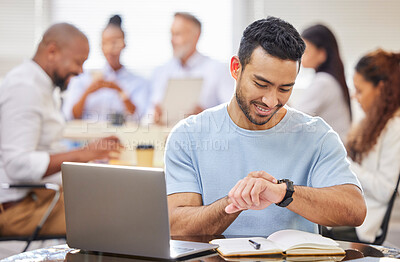 Buy stock photo Shot of a young businessman checking the time while working on a laptop in an office with his colleagues in the background