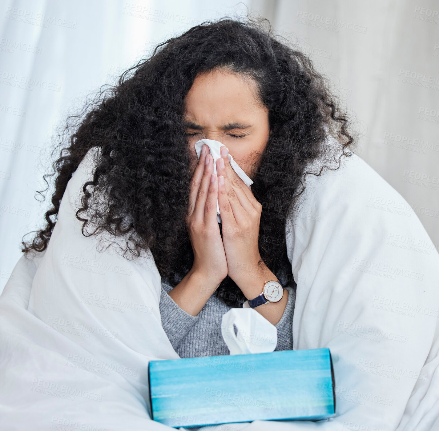 Buy stock photo Shot of an uncomfortable looking young woman blowing her nose while lying in bed at home