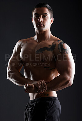 Buy stock photo Shot of athletic young man flexing his muscles while posing against a dark background
