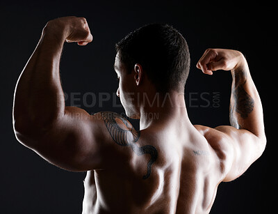 Buy stock photo Shot of athletic young man flexing his muscles while posing against a dark background