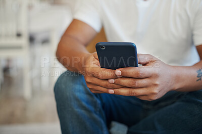 Buy stock photo Cropped shot of an unrecognizable man sitting alone on the sofa at home and using his cellphone