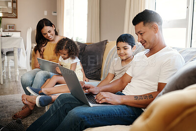 Buy stock photo Shot of a young family sitting on the sofa at home together and using technology