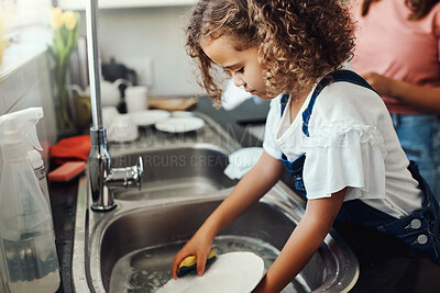 Buy stock photo Shot of an adorable young girl standing and washing the dishes in the kitchen sink at home