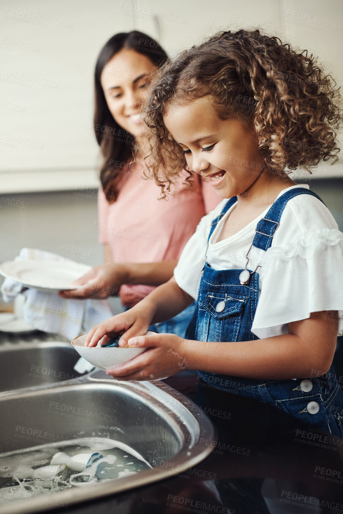 Buy stock photo Shot of an adorable young girl standing and helping her mother with the dishes in the kitchen at home