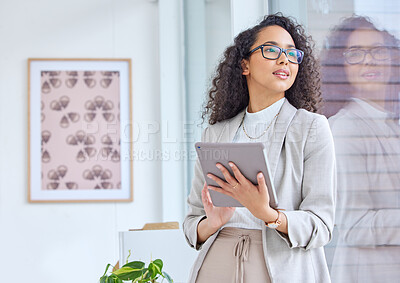Buy stock photo Shot of a young businesswoman using a digital tablet while looking out the window in an office