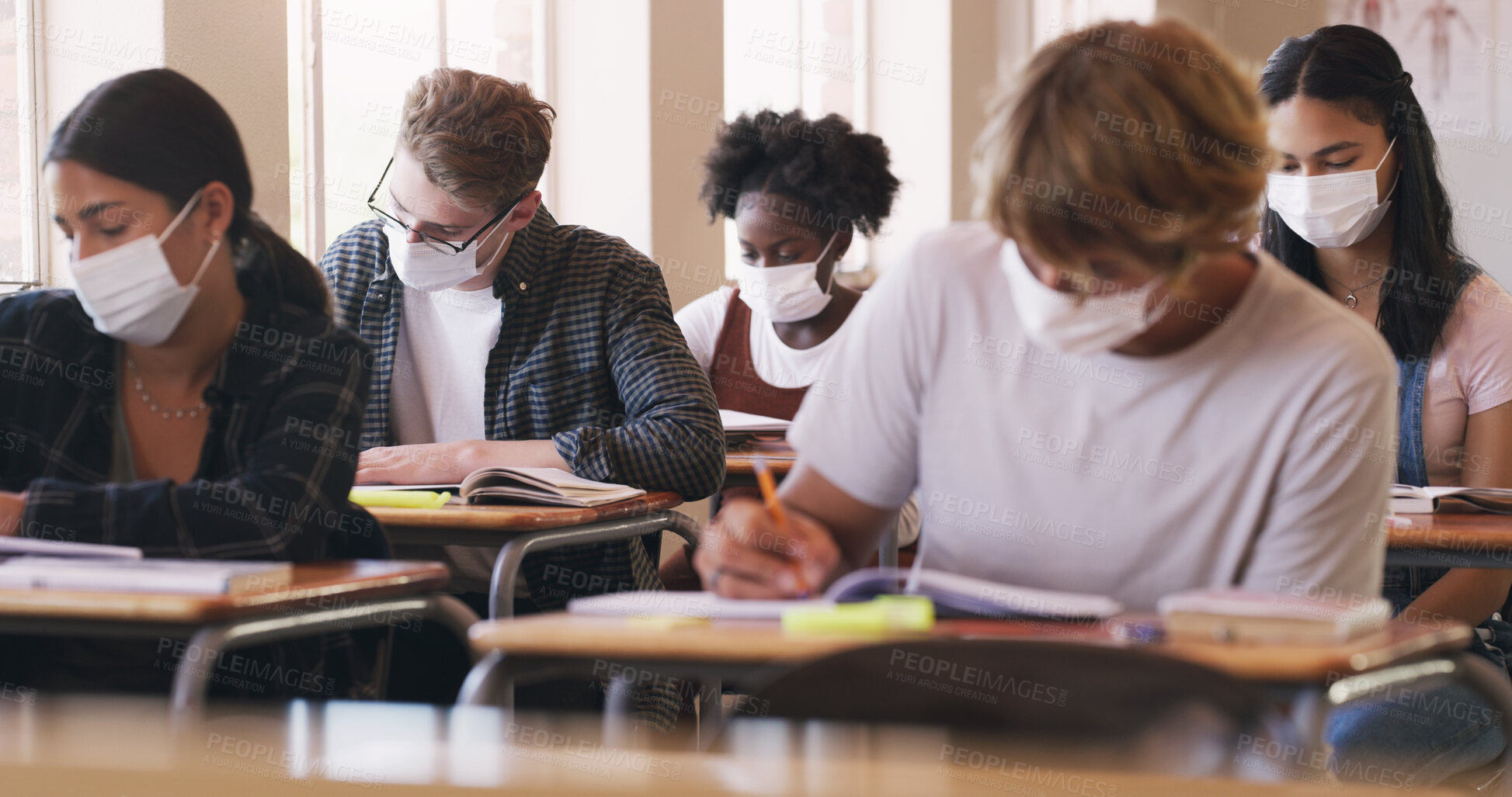 Buy stock photo Shot of masked teenagers writing an exam in a classroom