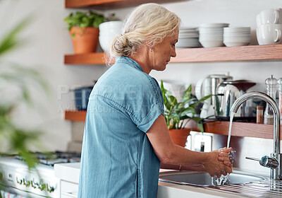 Buy stock photo Shot of a mature woman washing her hands in the kitchen sink at home
