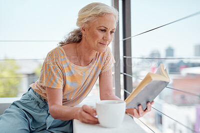 Buy stock photo Shot of a mature woman reading a book and having coffee on her balcony at home