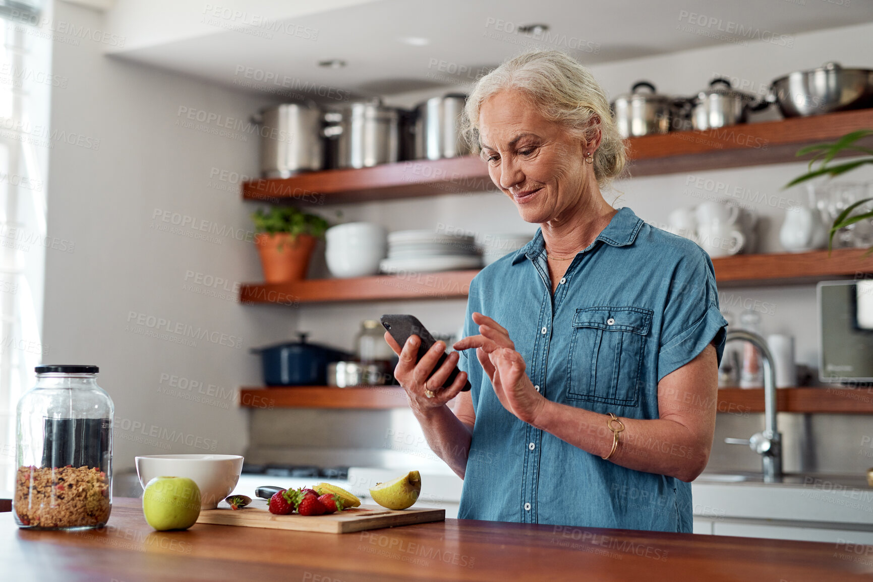 Buy stock photo Mature woman, kitchen and cellphone for mobile recipe, cooking and read for instructions online. Vegan, fruit and diet for health food in home, female person and internet for breakfast in retirement