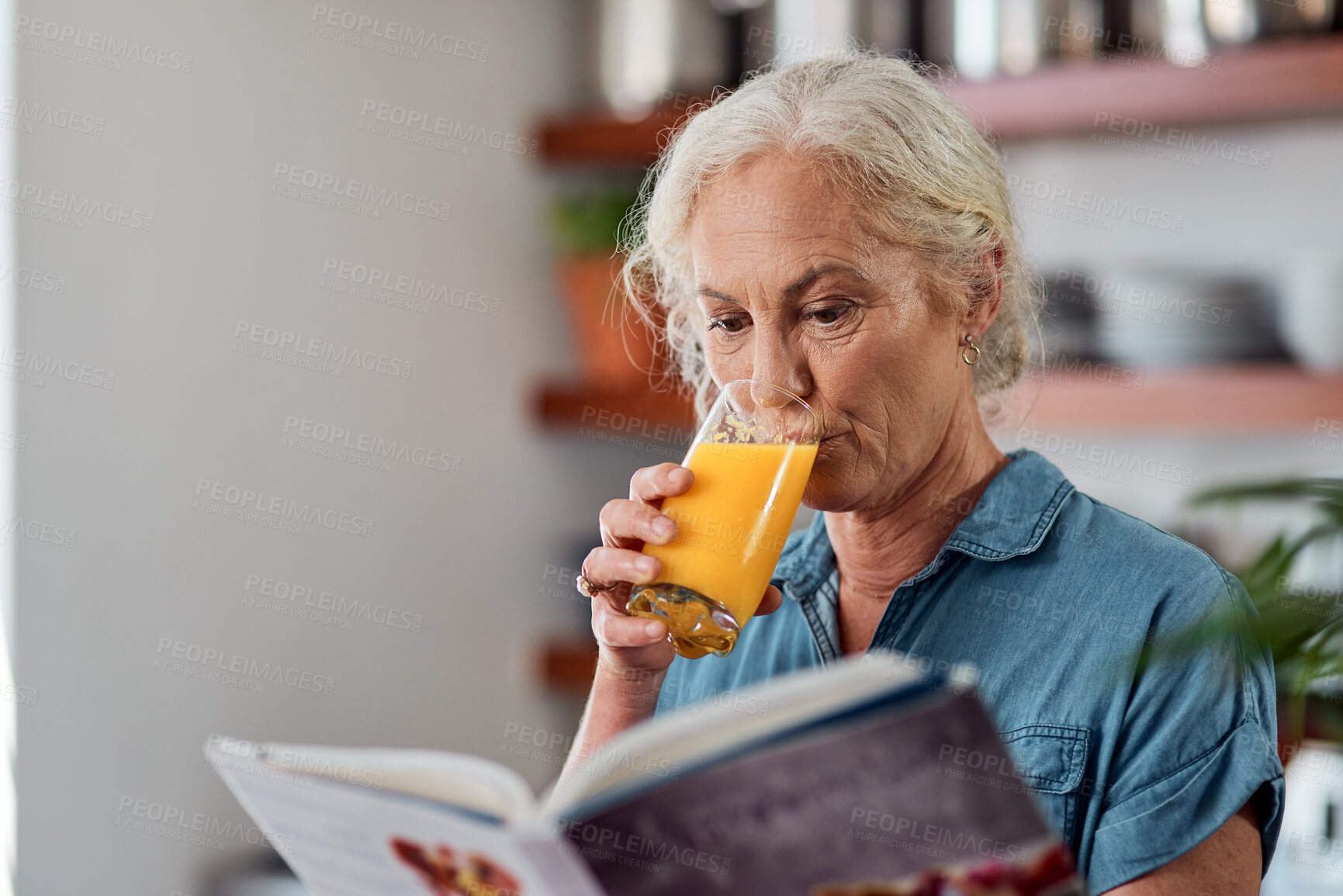 Buy stock photo Shot of a mature woman reading a book while having orange juice at home