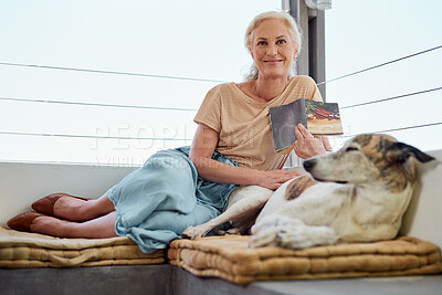 Buy stock photo Shot of a mature woman reading a book on her balcony with her dog next to her at home