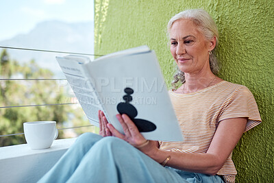 Buy stock photo Shot of a mature woman reading a book and having coffee on her balcony at home