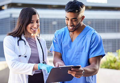 Buy stock photo Shot of two young doctors checking some paperwork while outside in the city