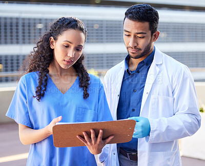Buy stock photo Shot of two young doctors checking some paperwork while outside in the city