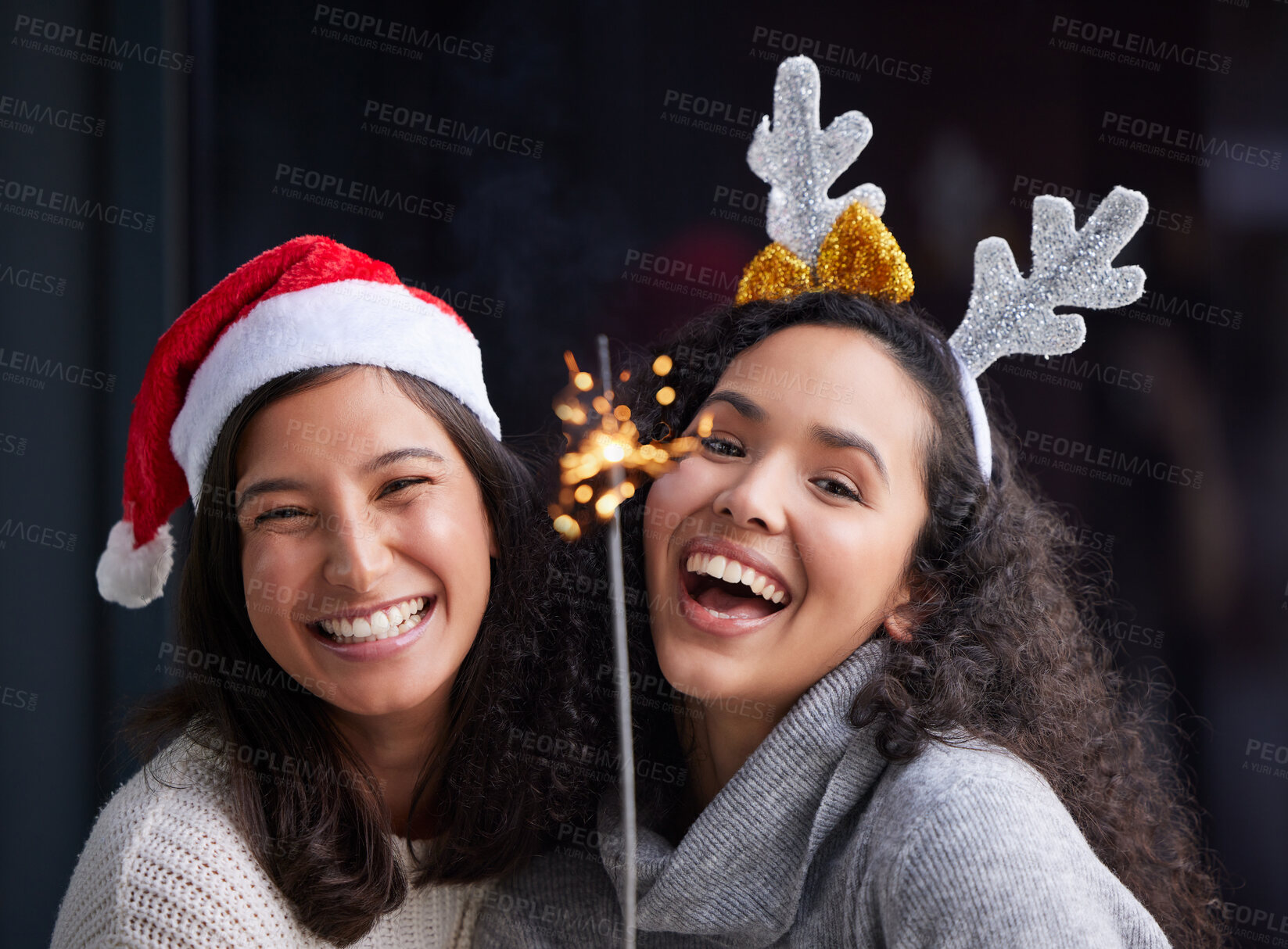 Buy stock photo Shot of two best friends standing together and holding up a sparker while celebrating Christmas
