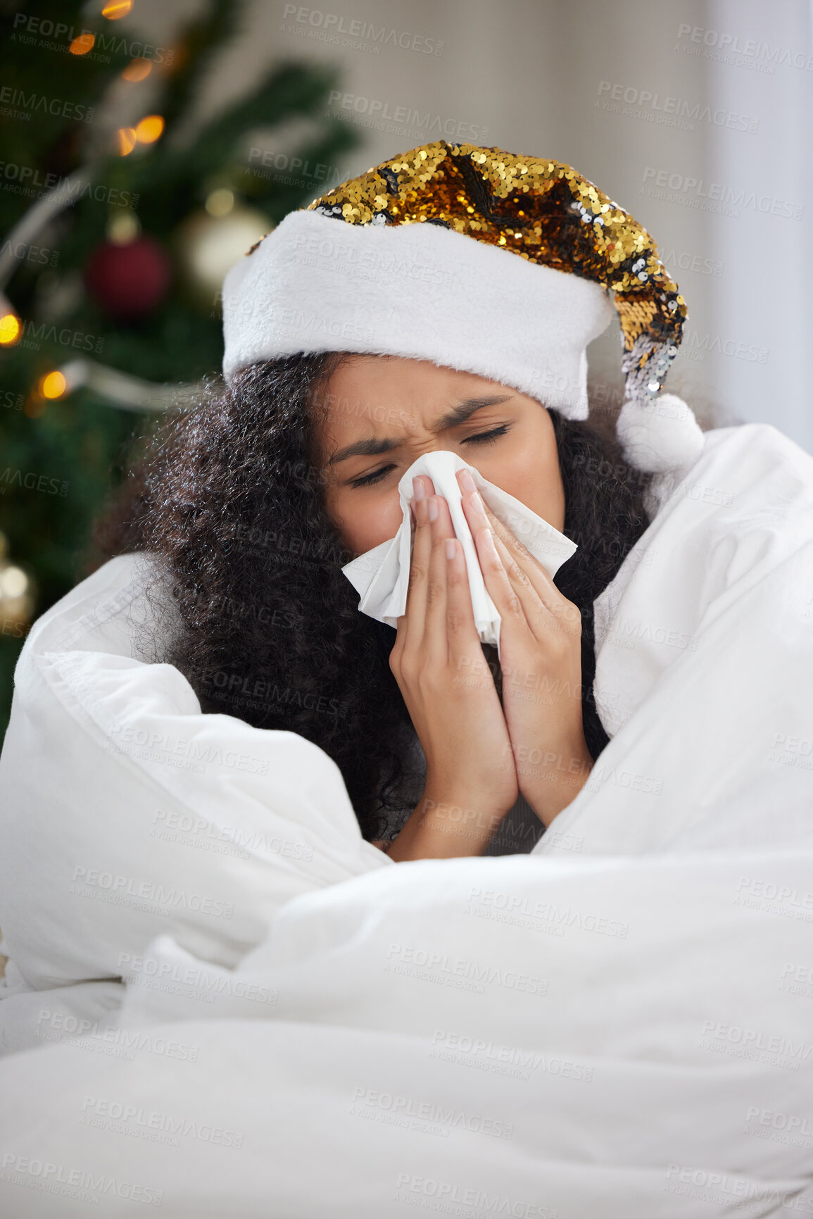 Buy stock photo Cropped shot of an attractive young woman blowing her nose while wearing a Christmas hat and lying on the sofa at home