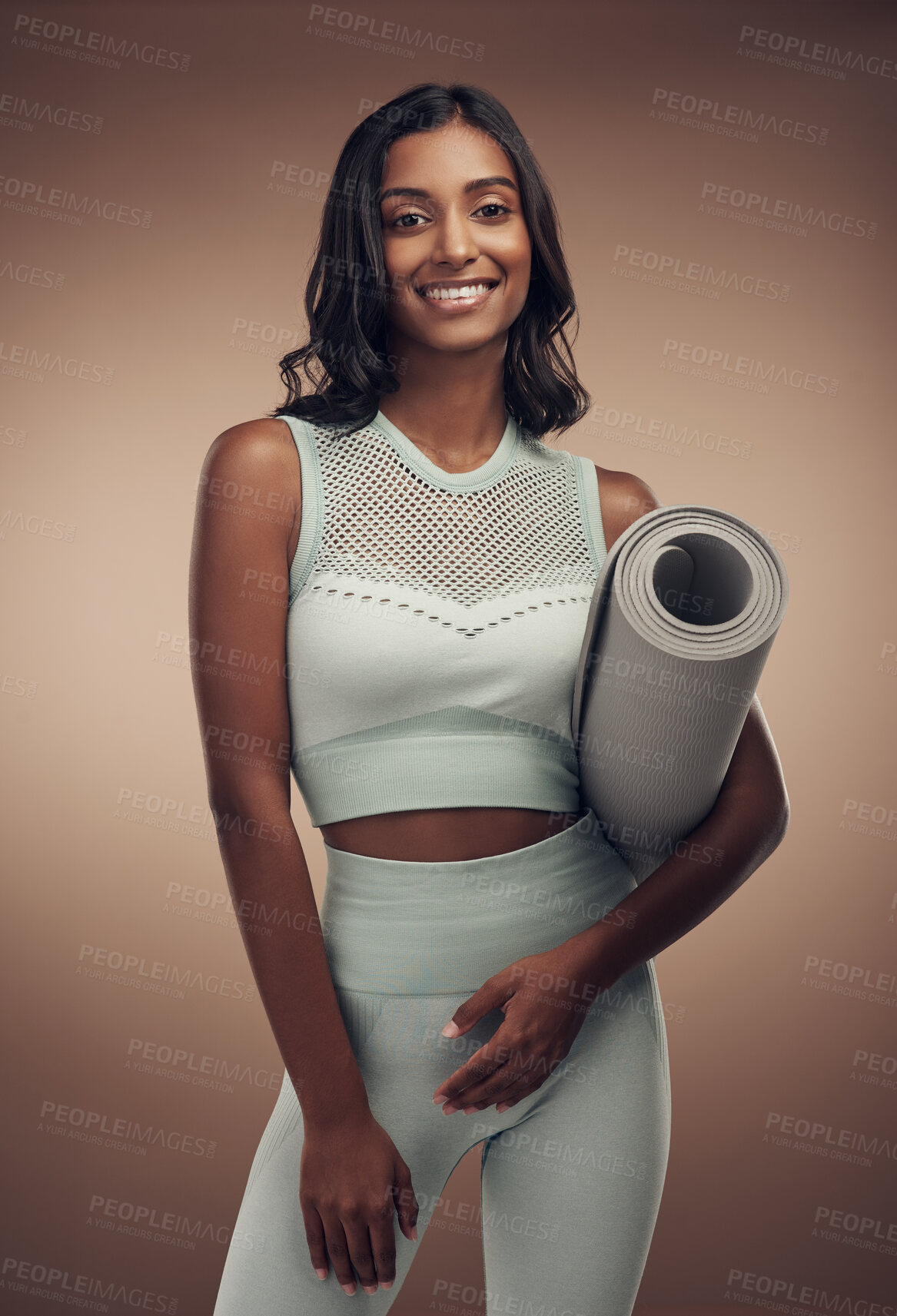 Buy stock photo Shot of an attractive young woman standing alone in the studio and holding a yoga mat