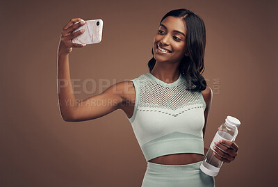 Buy stock photo Shot of an attractive young woman standing alone in the studio and using her cellphone to take selfies