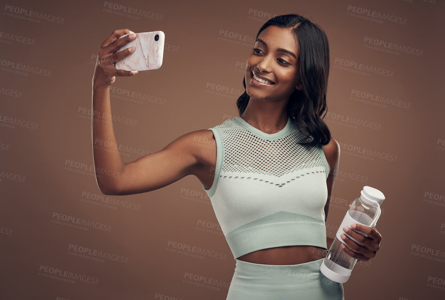 Buy stock photo Shot of an attractive young woman standing alone in the studio and using her cellphone to take selfies