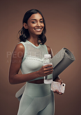 Buy stock photo Shot of a young woman standing in the studio and holding a yoga mat and water bottle after working out