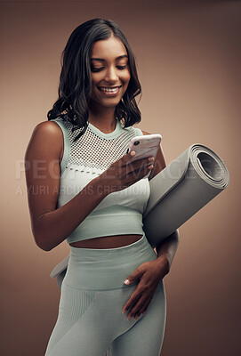 Buy stock photo Shot of an attractive young woman standing alone in the studio and using her cellphone after a workout