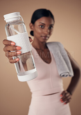 Buy stock photo Shot of a young woman standing alone in the studio and holding a water bottle after working out