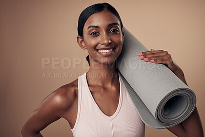 Buy stock photo Shot of an attractive young woman standing alone in the studio and holding a yoga mat