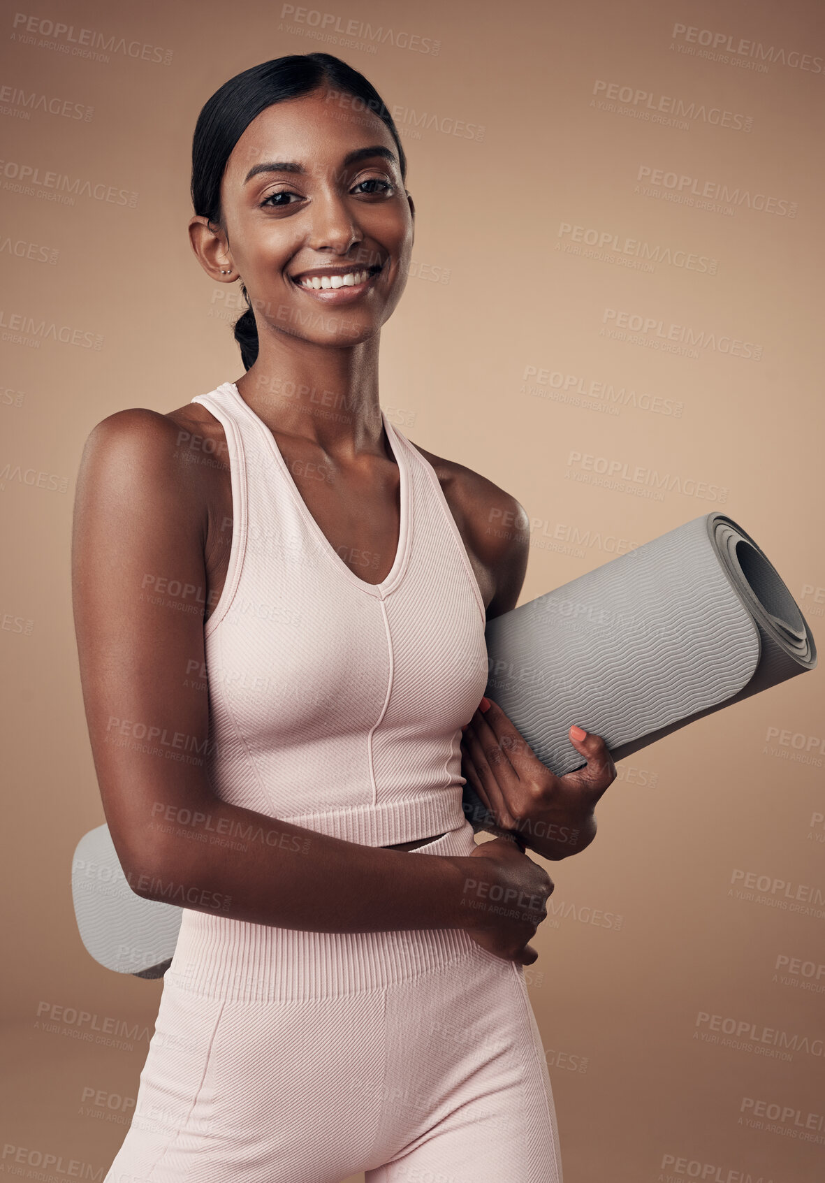 Buy stock photo Shot of an attractive young woman standing alone in the studio and holding a yoga mat