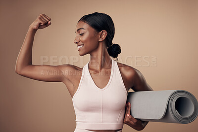Buy stock photo Shot of an attractive young woman standing alone in the studio and flexing her muscles while holding a yoga mat