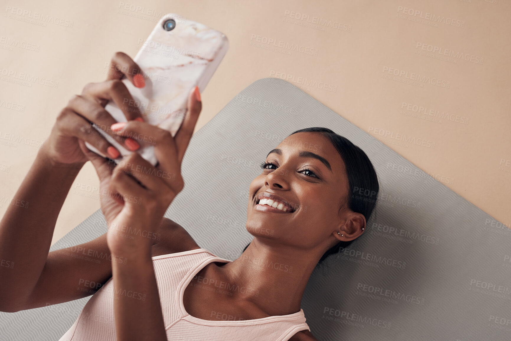 Buy stock photo Shot of an attractive young woman lying down on a yoga mat and using her cellphone after working out