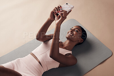 Buy stock photo Shot of an attractive young woman lying down on a yoga mat and using her cellphone after working out