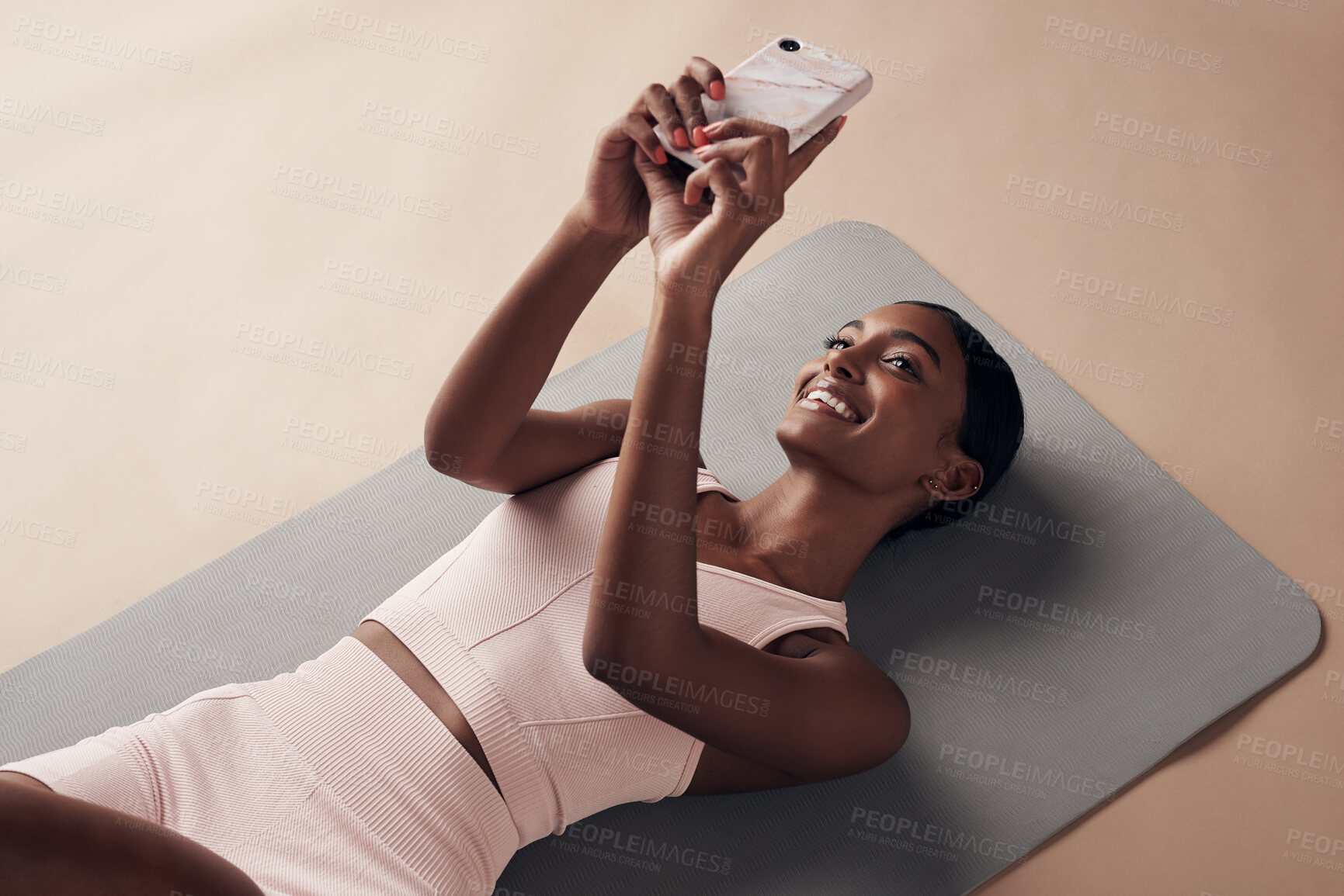 Buy stock photo Shot of an attractive young woman lying down on a yoga mat and using her cellphone after working out