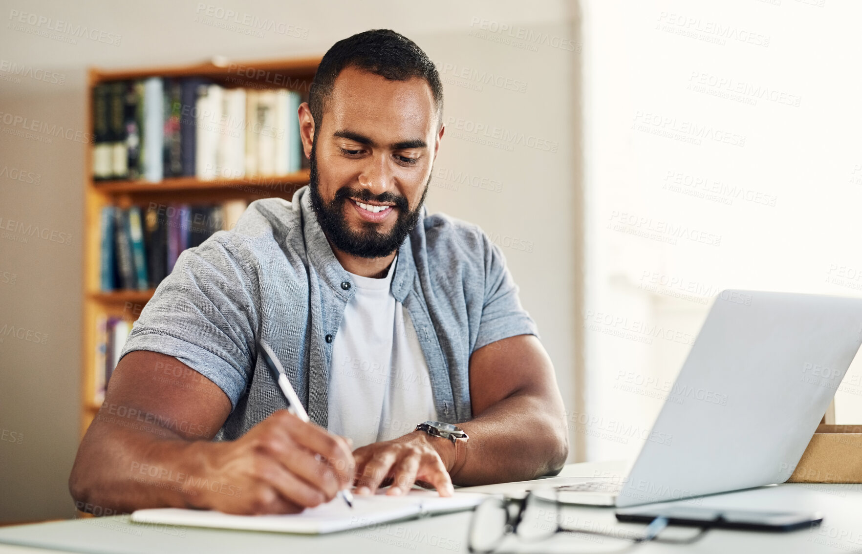 Buy stock photo Shot of a young male businessman working from home and writing in his notebook