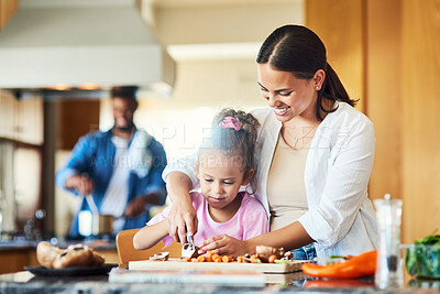 Buy stock photo Shot of a little girl assisting her mother with chopping vegetables at home