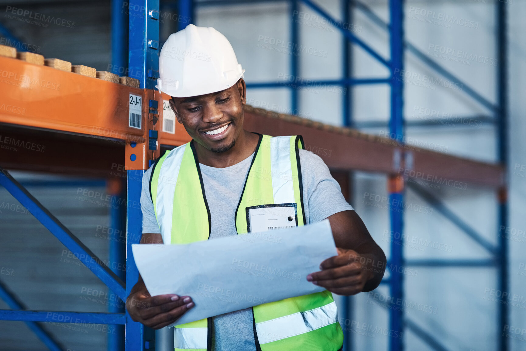 Buy stock photo Shot of a handsome young contractor standing in the warehouse and reading paperwork