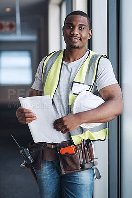 Buy stock photo Shot of a handsome young contractor standing alone in a building and holding the floor plan