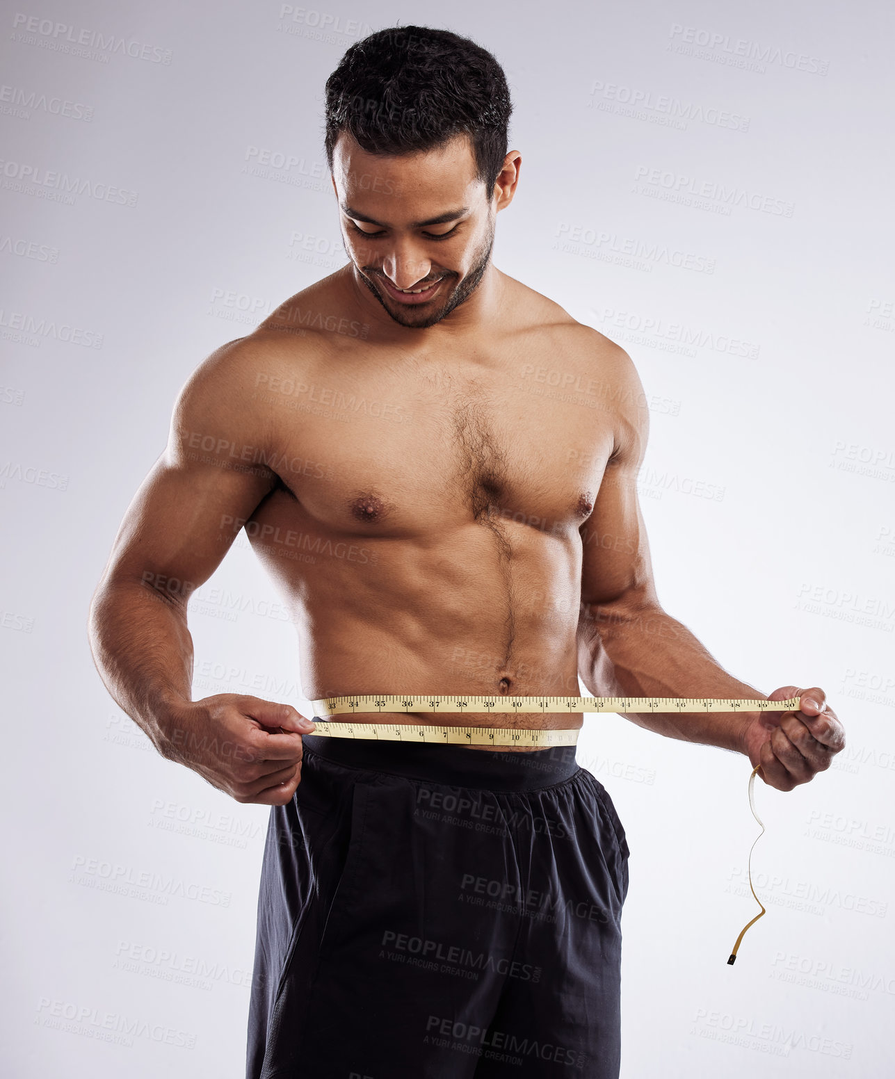 Buy stock photo Shot of a man measuring his waist using a measuring tape against a studio background